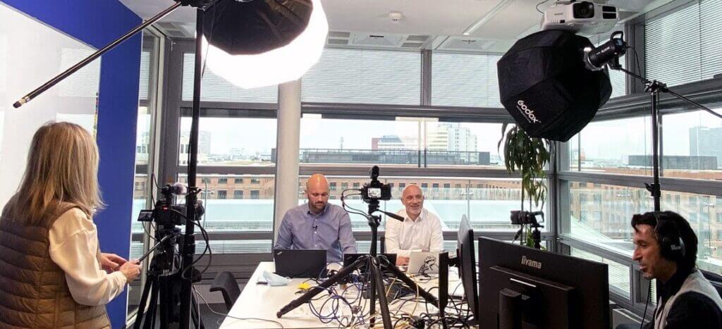 4 people are sitting in an office. The technology for transmitting the recordings is set up there, such as light and sound.