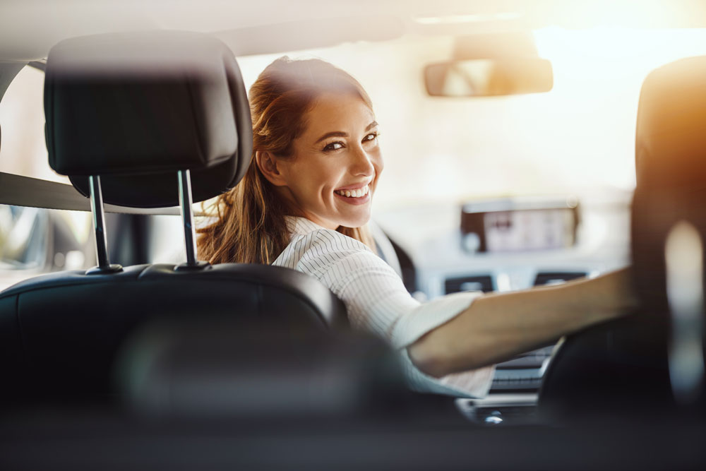 Eine Frau sitzt am Steuer eines Autos und blickt fröhlich über die Schulter auf den Rücksitz. Auch die Autoindustrie bietet Abo-Modelle an. 