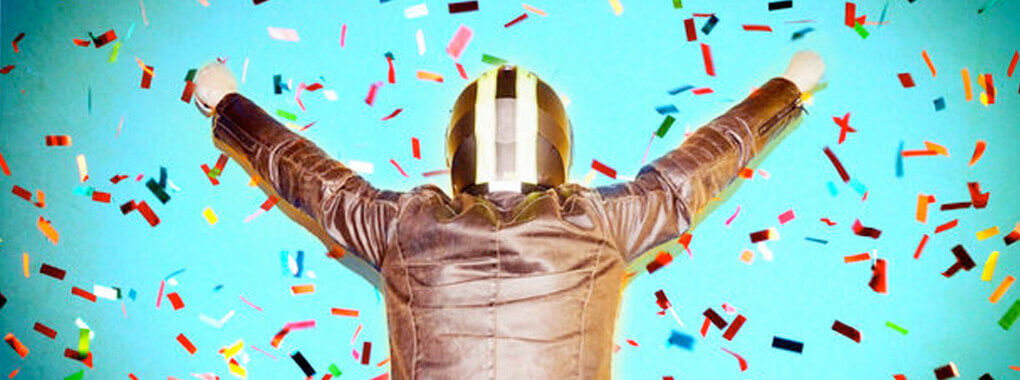 A person with a helmet and leather jacket can be seen from behind. Colorful confetti trickles down on the person.
